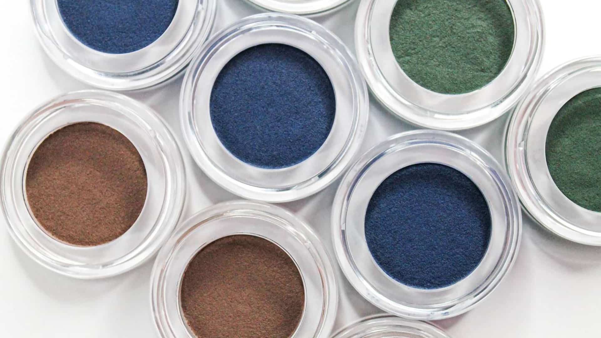 Top close-up of 9 colorful eyeshadows (brown, blue, green) in round clear pots