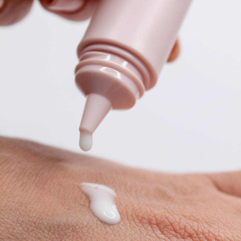 Pink dropper releasing white primer onto a hand, close-up view
