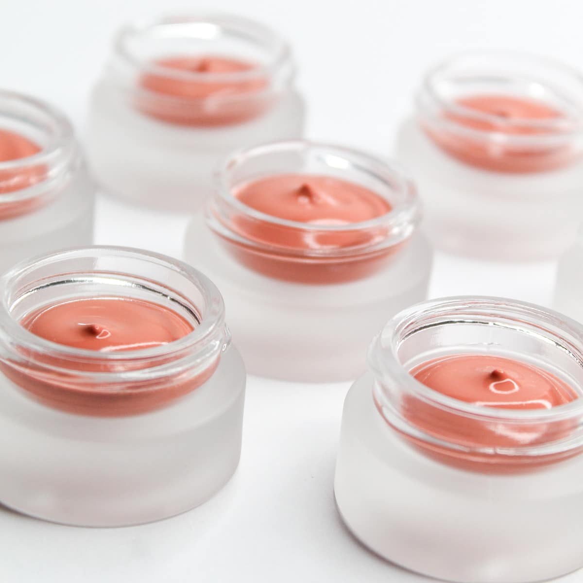 Coral skincare-infused primer in open glass jars on white background
