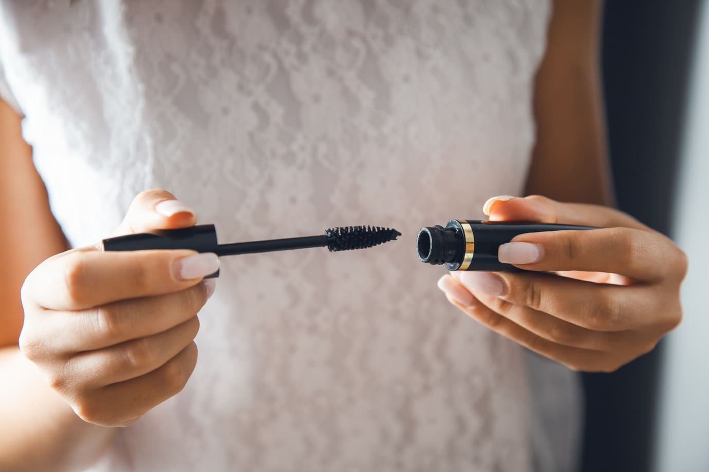 Close-up of hands holding mascara brush and open mascara tube