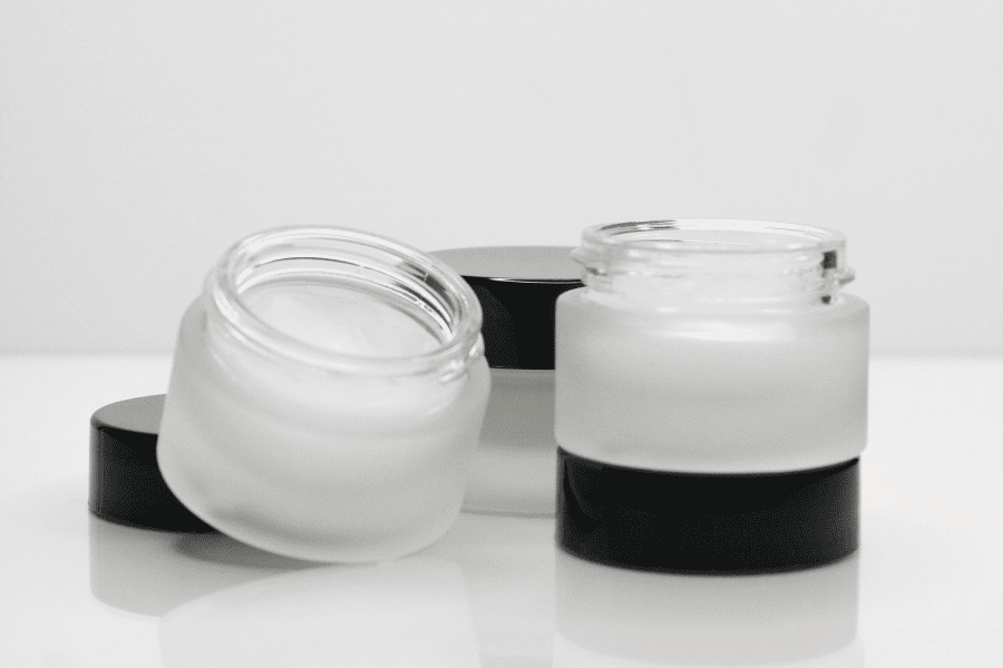 Two open frosted glass jars in front reveal the primer’s cloud-like texture.