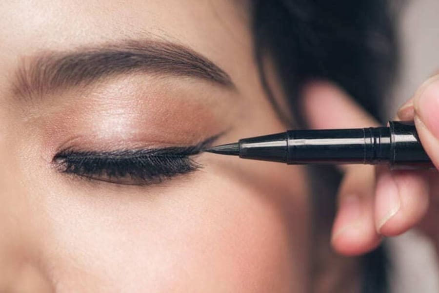 Close-up of a woman getting black eyeliner applied to her upper lash line