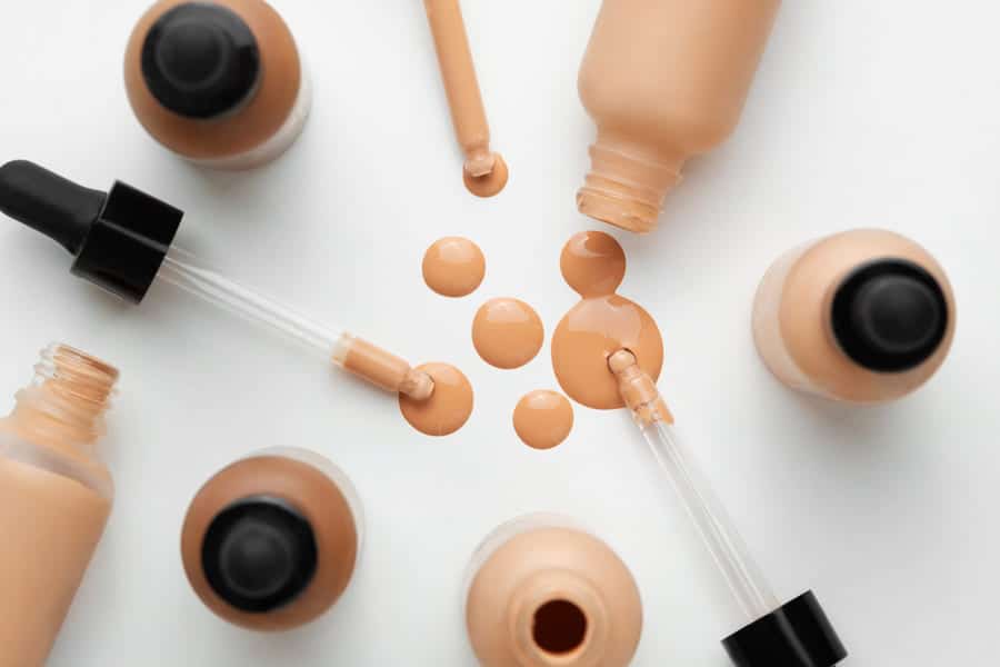 Skin tint bottles and droppers with liquid makeup spilled onto a white surface.