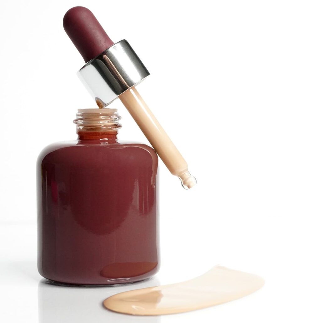 Dropper bottle with beige liquid foundation and swatch on white background