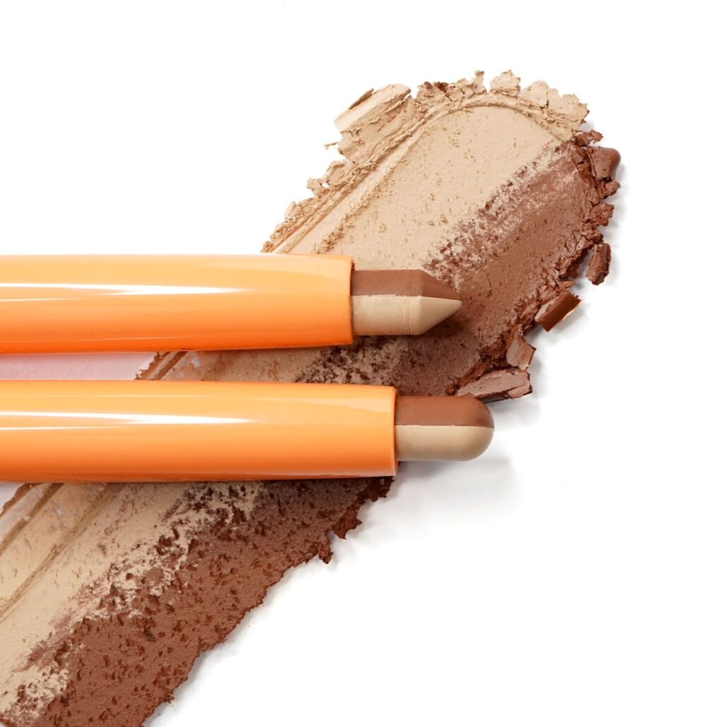 Dual-tip eyeshadow crayons on beige and brown texture swatches